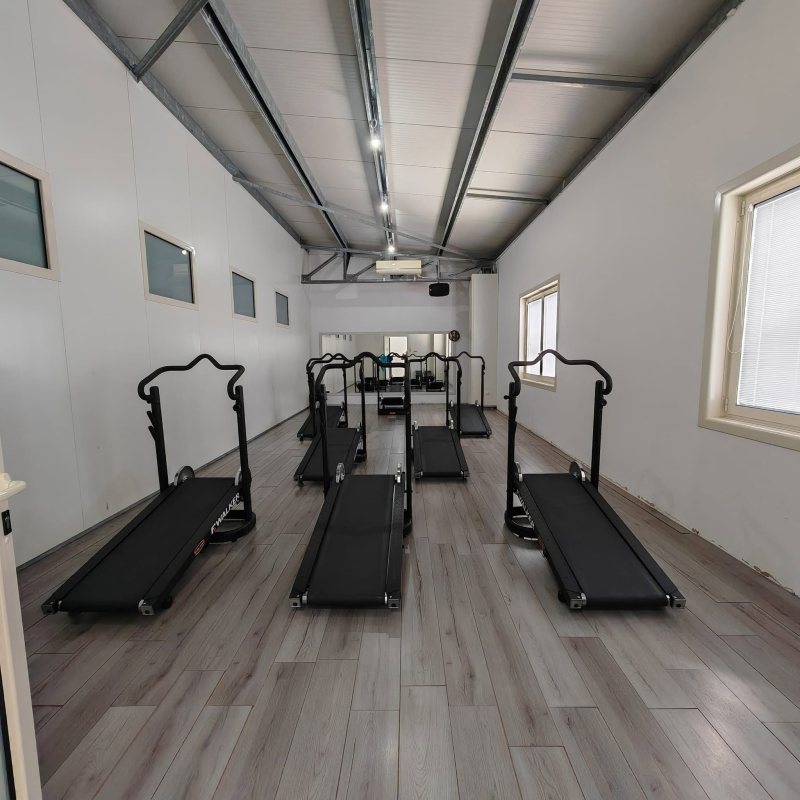 Palestra interna vuota con diversi tapis roulant neri in una lunga stanza bianca.