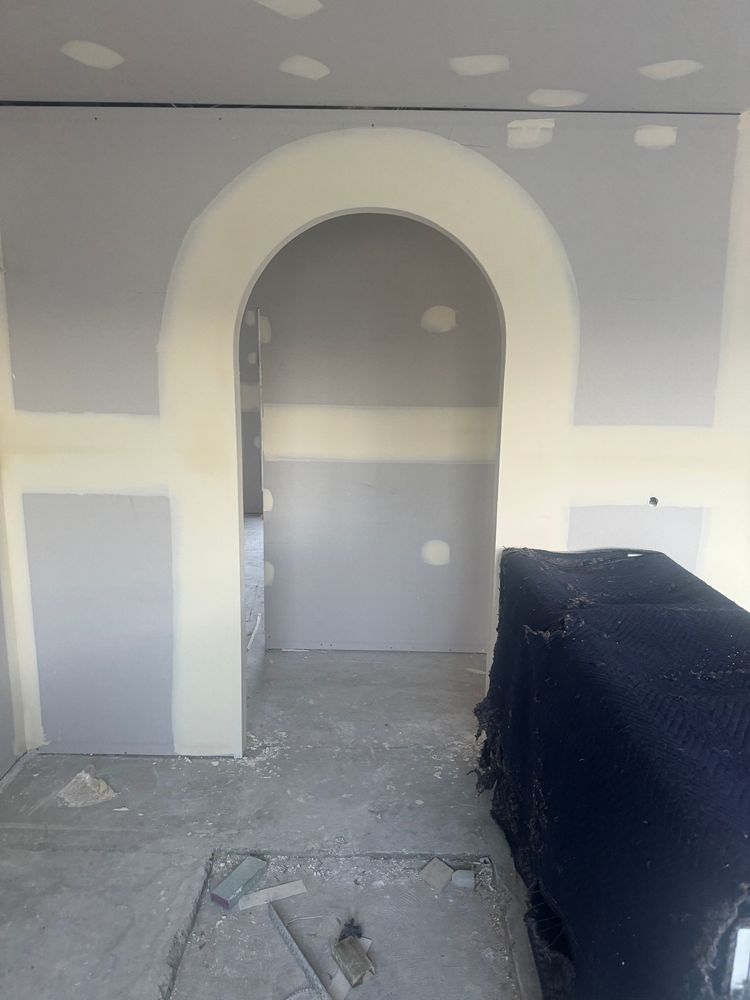 Unfinished room with gray drywall, arched doorway, and a covered object on the right.