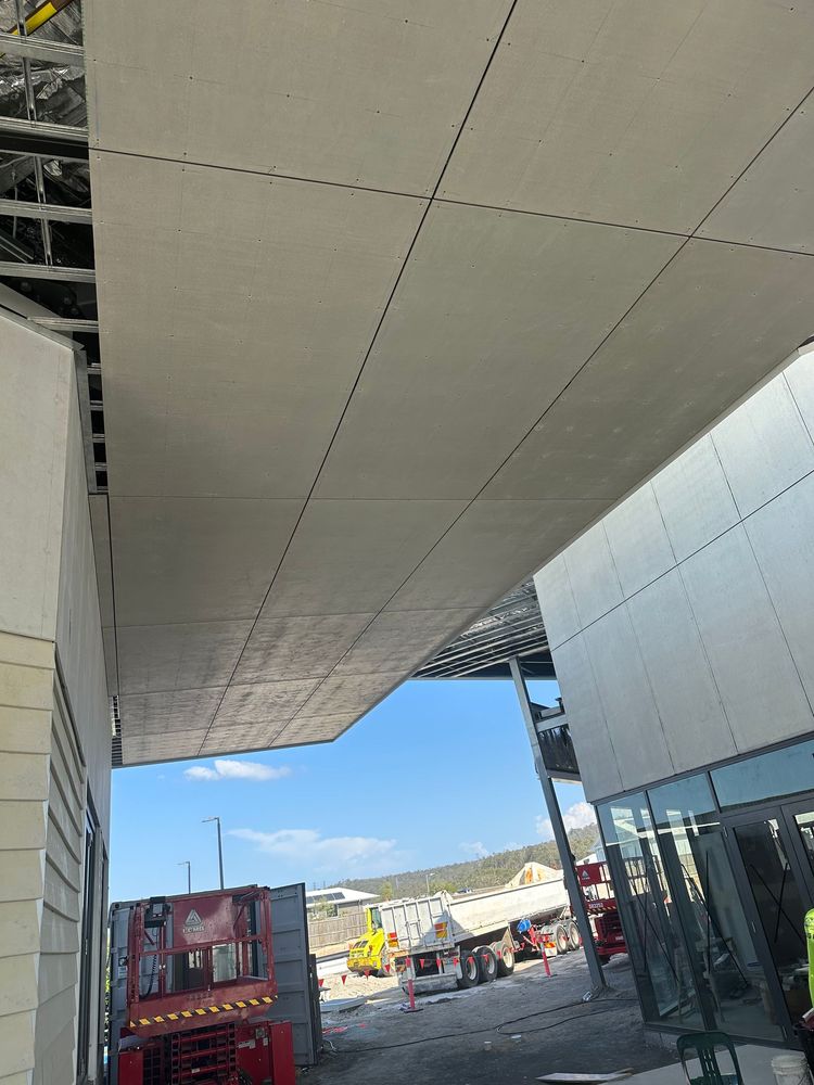 Covered outdoor walkway beside a modern building, with a red utility vehicle and blue sky in the distance.