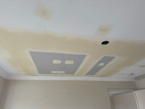 Ceiling under repair with patched drywall, primer spots, and a light fixture hole