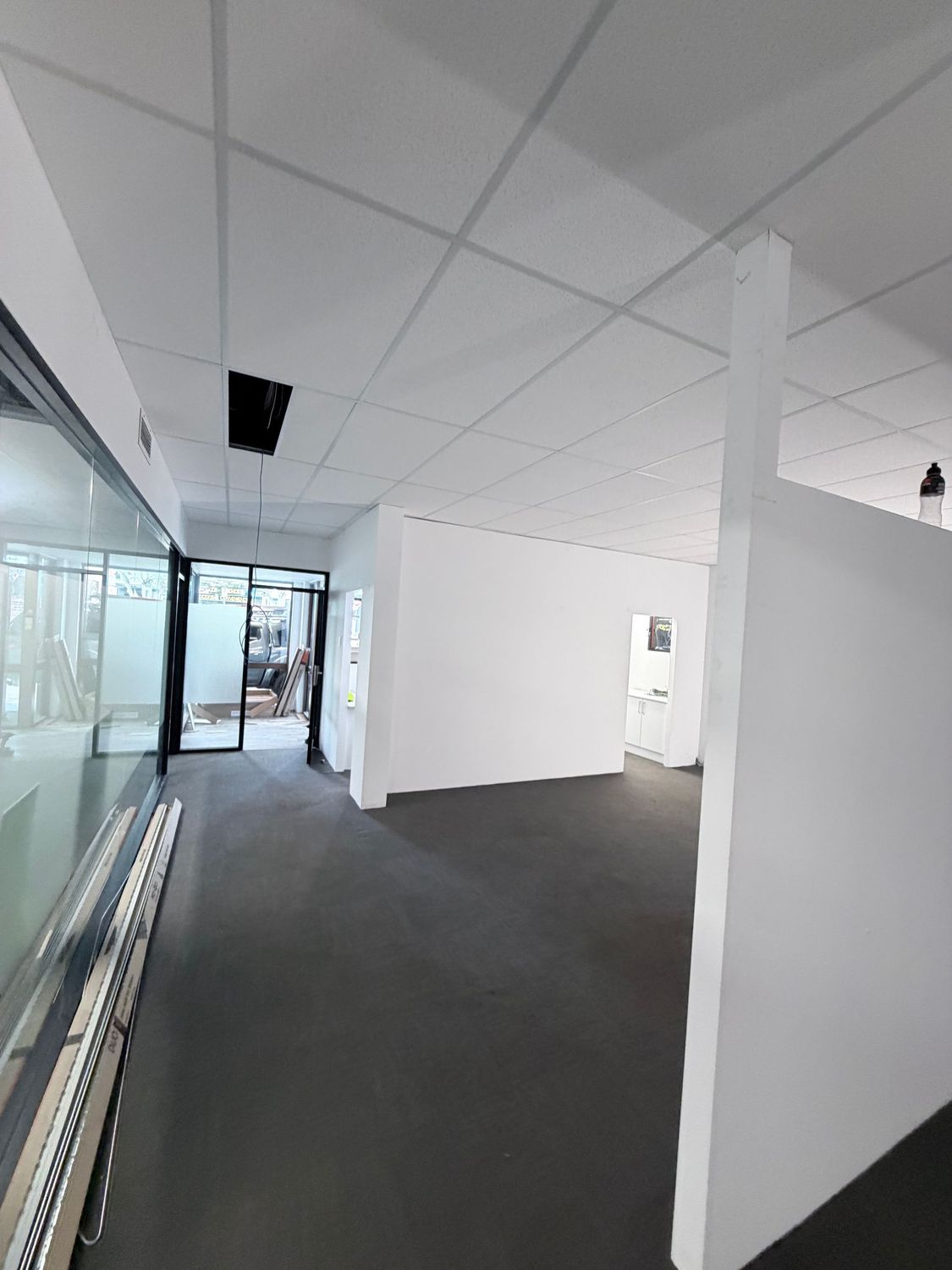 Empty office hallway with white walls, gray carpet, glass partitions, and ceiling panels