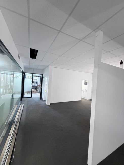 Empty office hallway with white walls, gray carpet, glass partitions, and ceiling panels