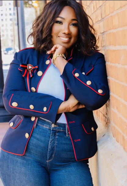 Woman in blue jacket and jeans, smiling, leaning against a brick wall.