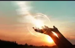 Hands reaching upward toward a beam of light in a colorful sunset.