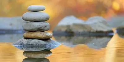 Stack of smooth stones balanced in calm water. Golden and blurred background.