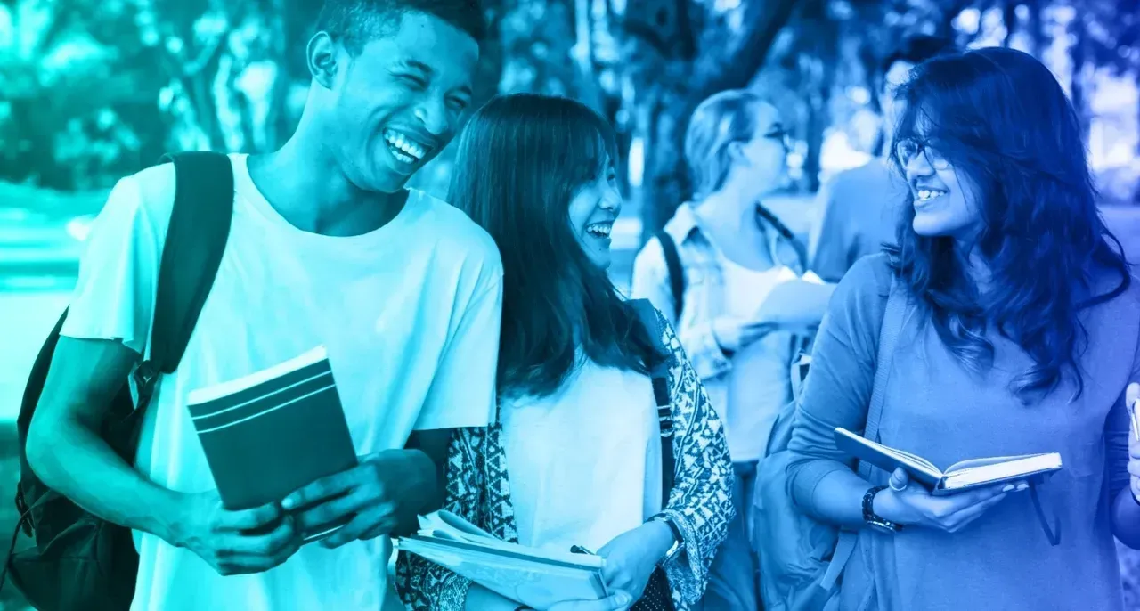 Smiling students walk together on a campus path, holding books. Cyan and blue tones.