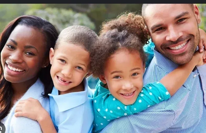 Family smiling together outdoors; parents embrace children.