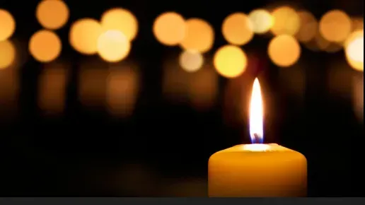Yellow candle flame against a dark background with blurred yellow lights, evoking warmth.