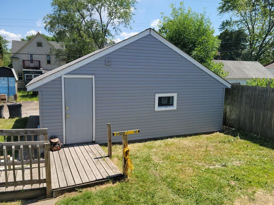A gray garage with a ramp leading to it is in the backyard of a house.