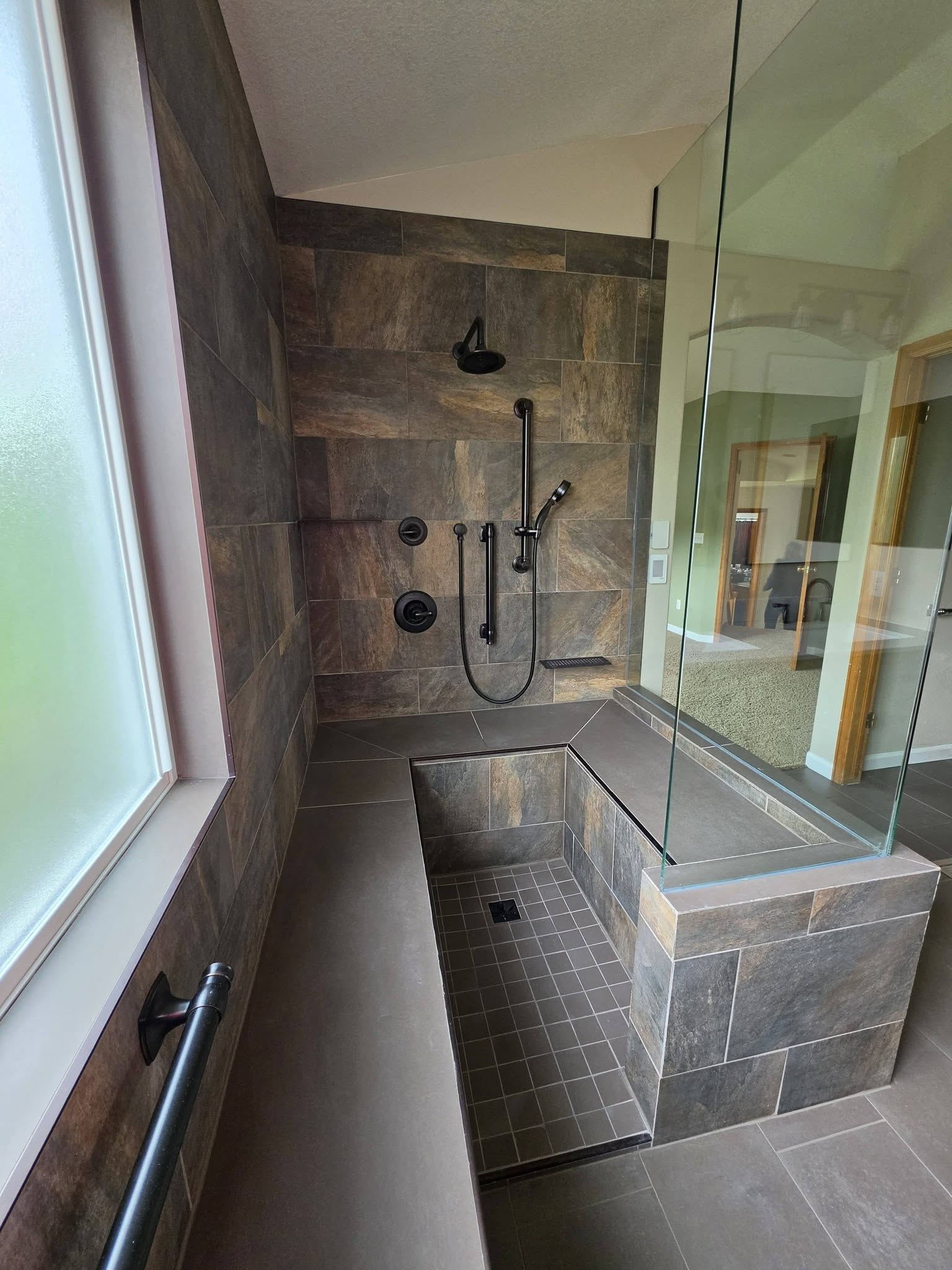 Modern tiled bathroom with a walk-in shower, black fixtures, and a glass partition