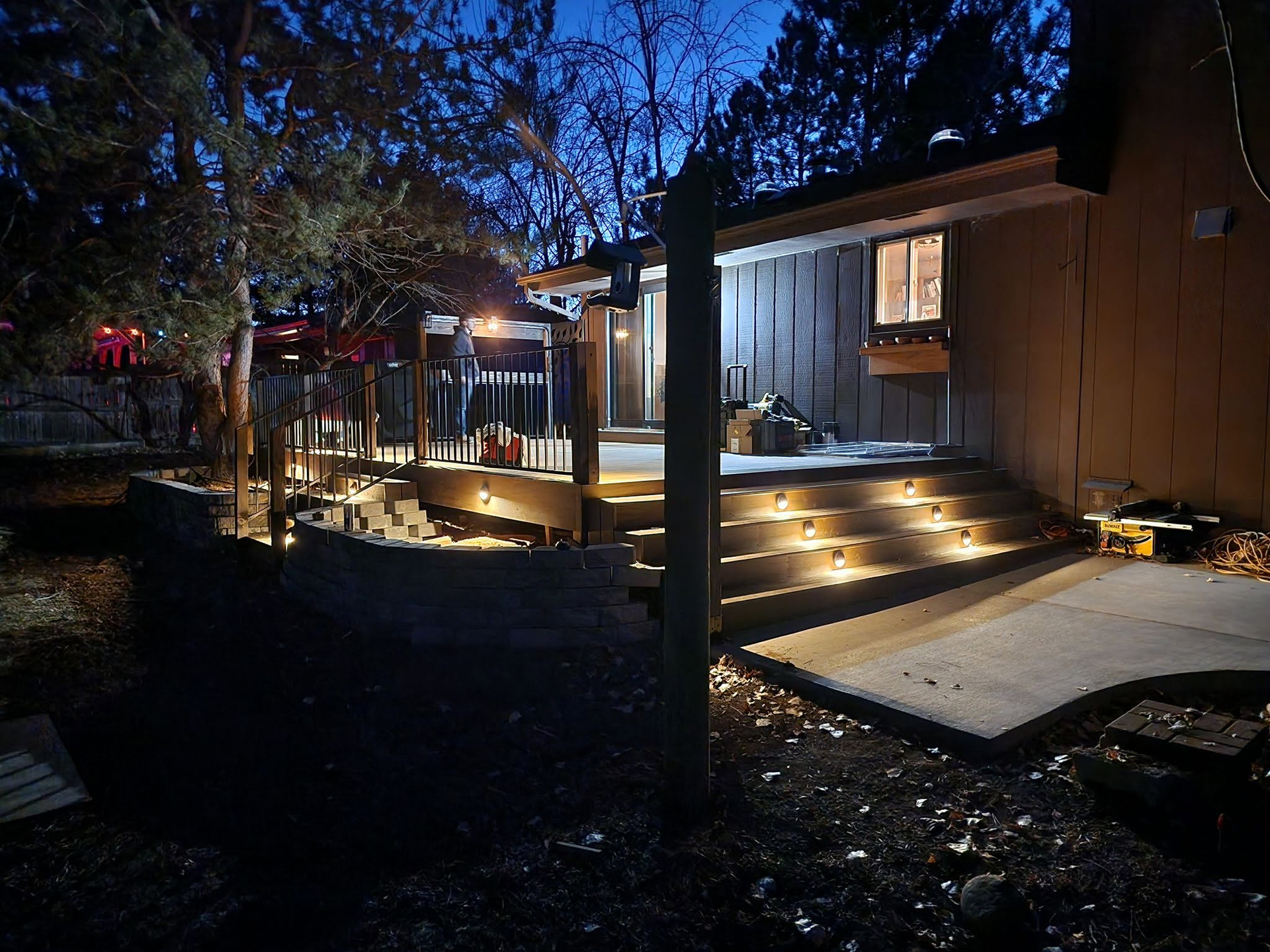 Nighttime wooden deck and porch with warm step lights beside a cabin under trees