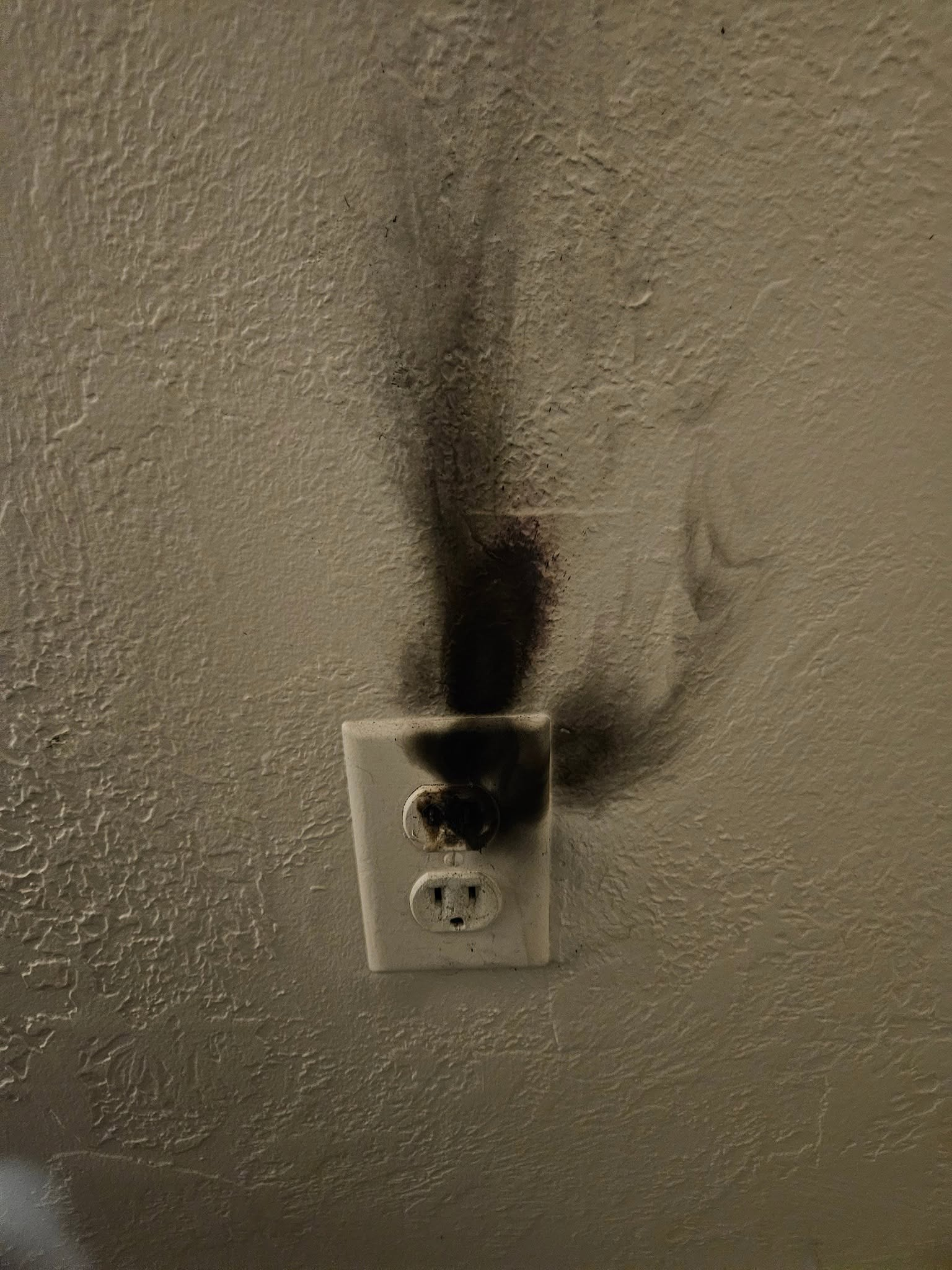 Burned electrical outlet on a textured wall with smoke stains above it