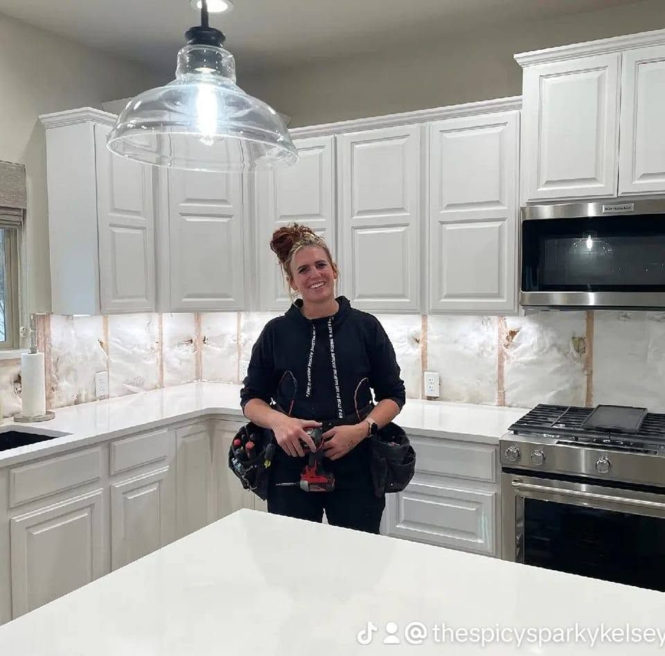 Woman standing in a bright white kitchen, smiling and holding a red drink bottle.