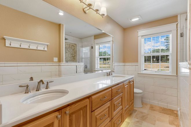 Bright bathroom with double vanity, large mirror, window, and white tile walls