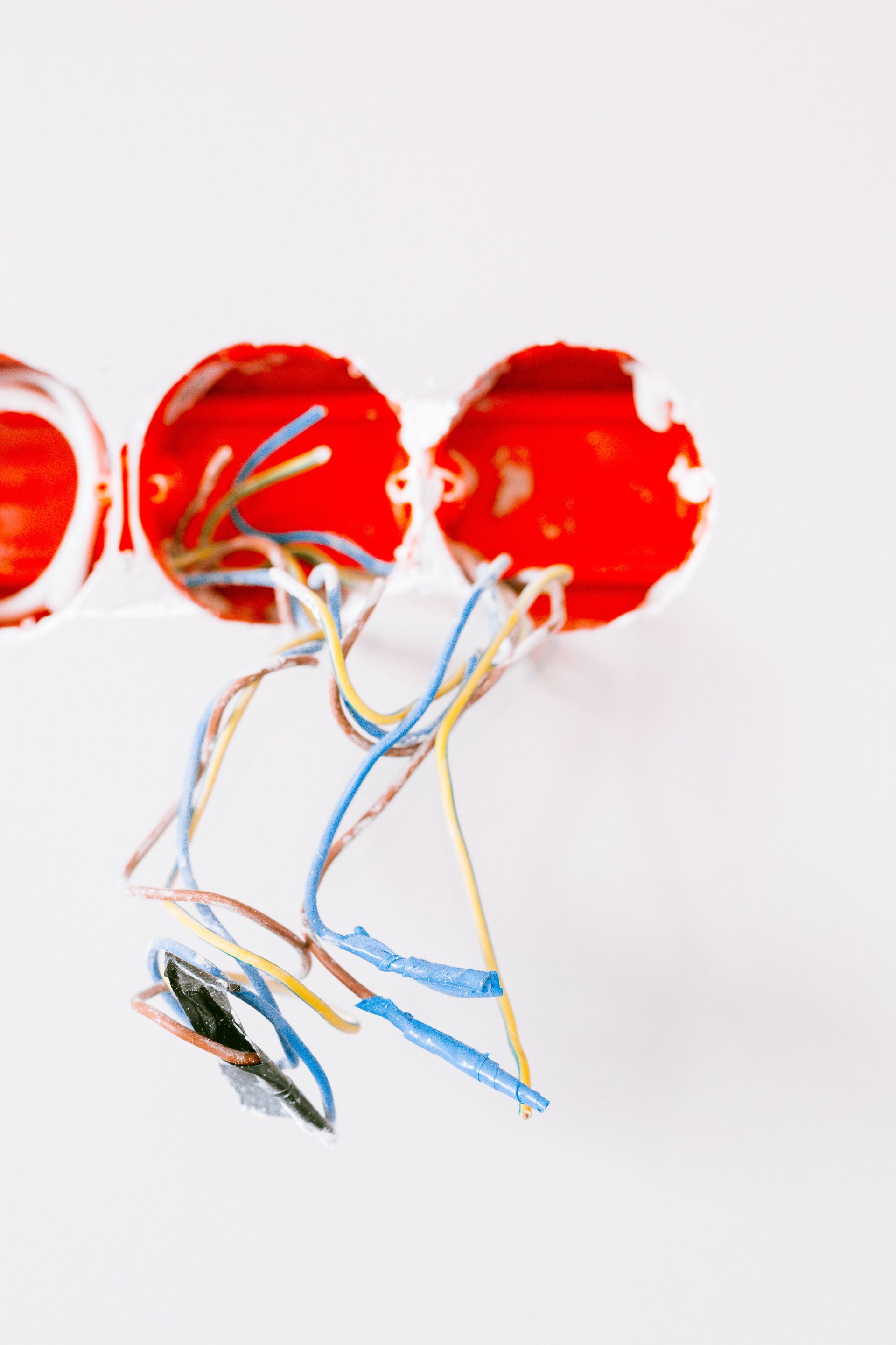 Three red balloon-like shapes with colorful wires hanging below on a white background