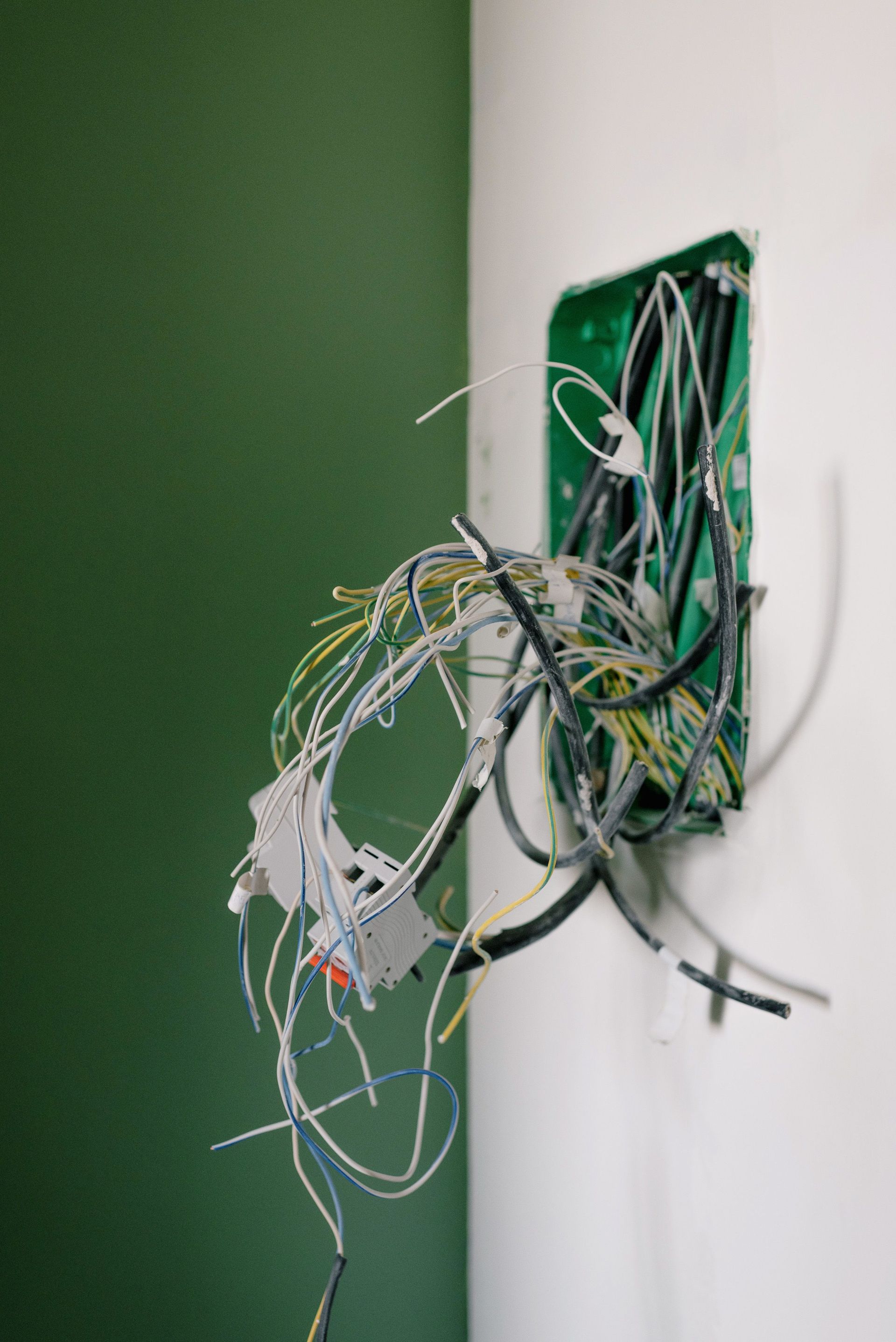 Exposed bundle of tangled wires protruding from a wall-mounted electrical box on a green and white wall