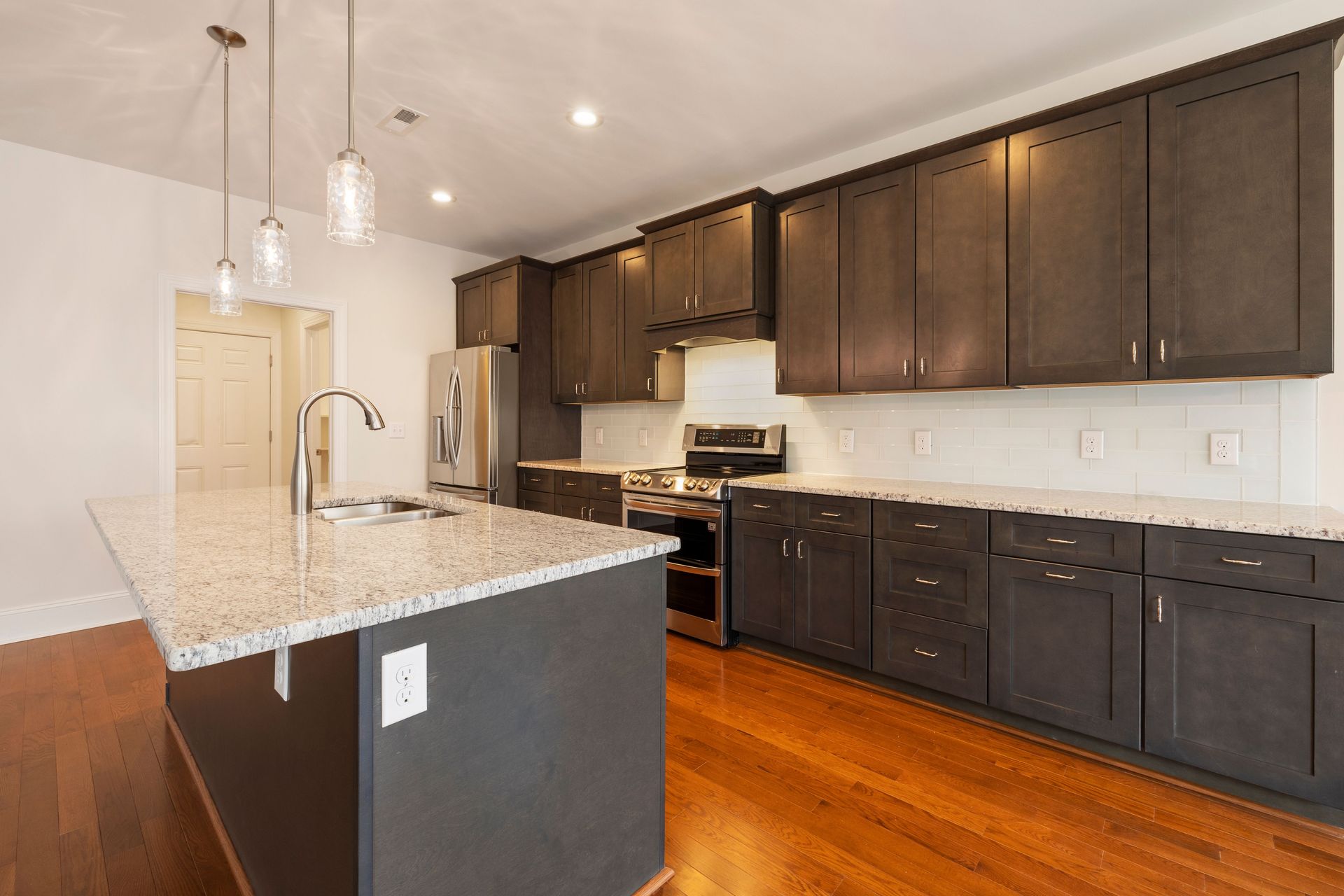 Bright modern kitchen with dark cabinets, white countertops, hardwood floors, and stainless steel appliances