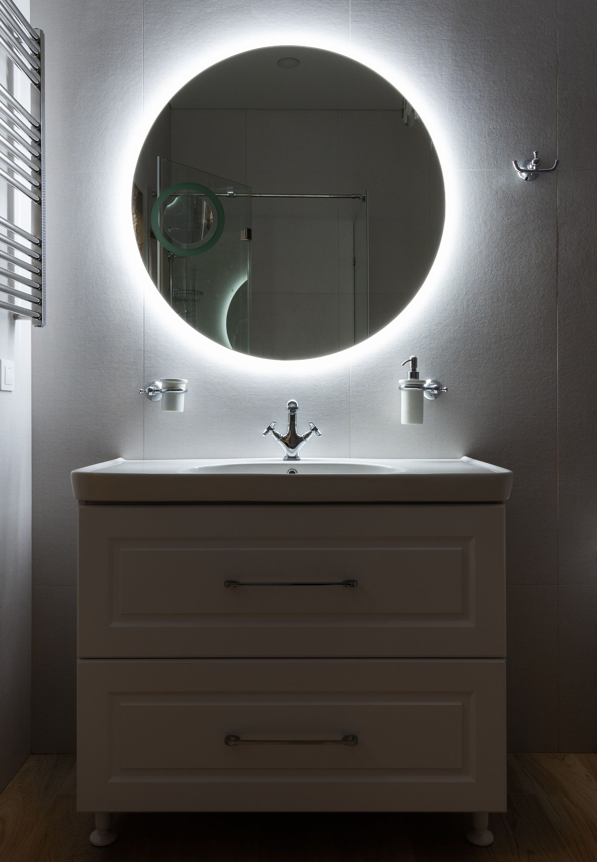 Modern bathroom vanity with round lit mirror and white sink against textured gray wall