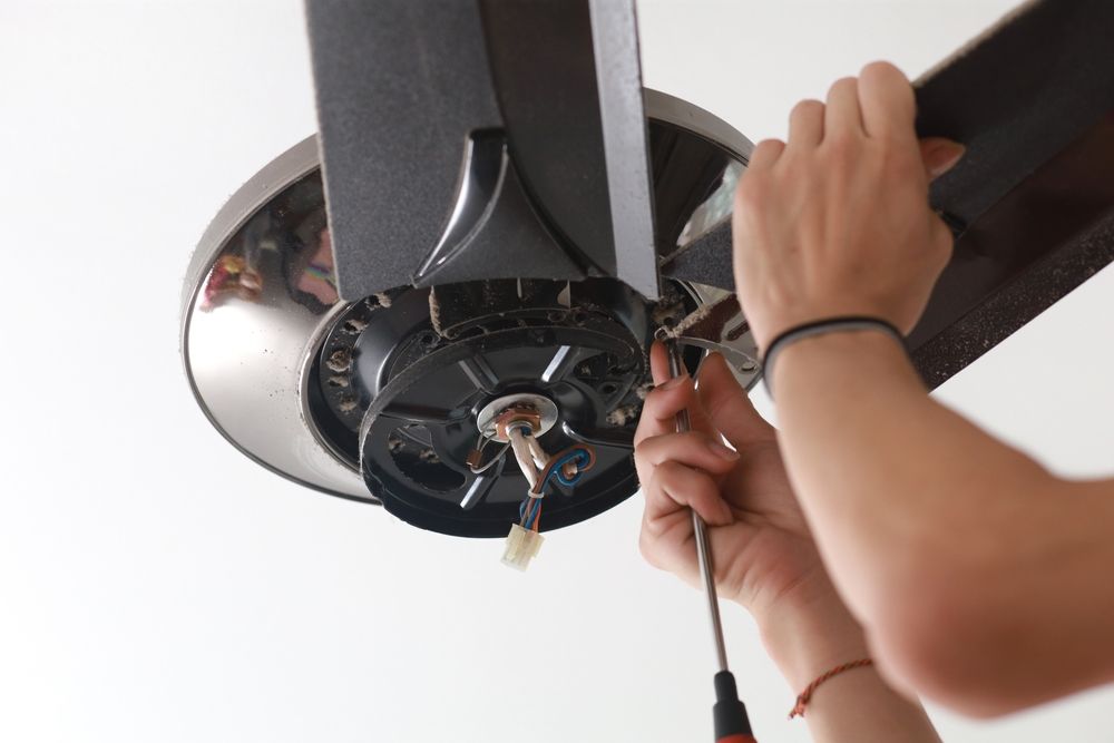 Hands repairing a ceiling fan with a screwdriver and red wire