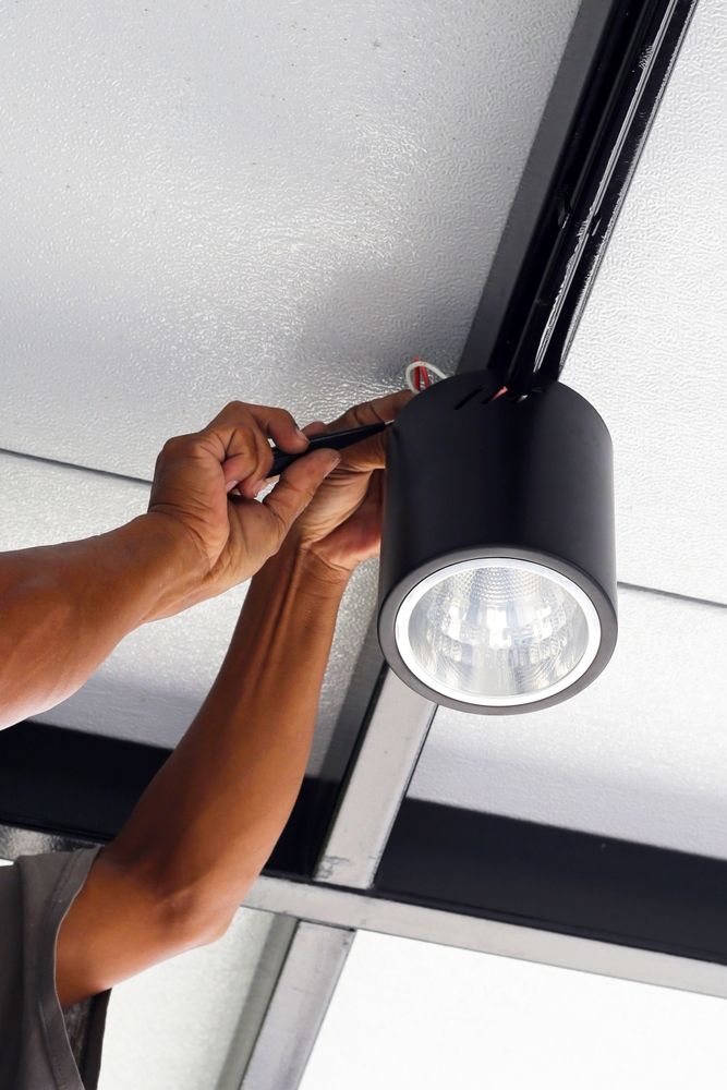 Hands installing a black track light on a white ceiling