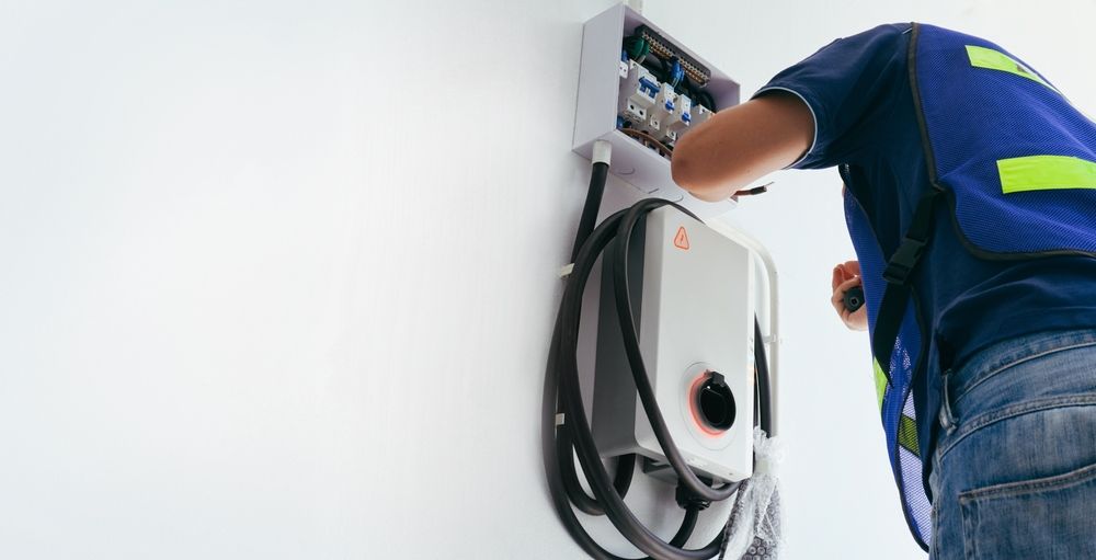 Technician installing a wall-mounted electric vehicle charger with cables in a white room