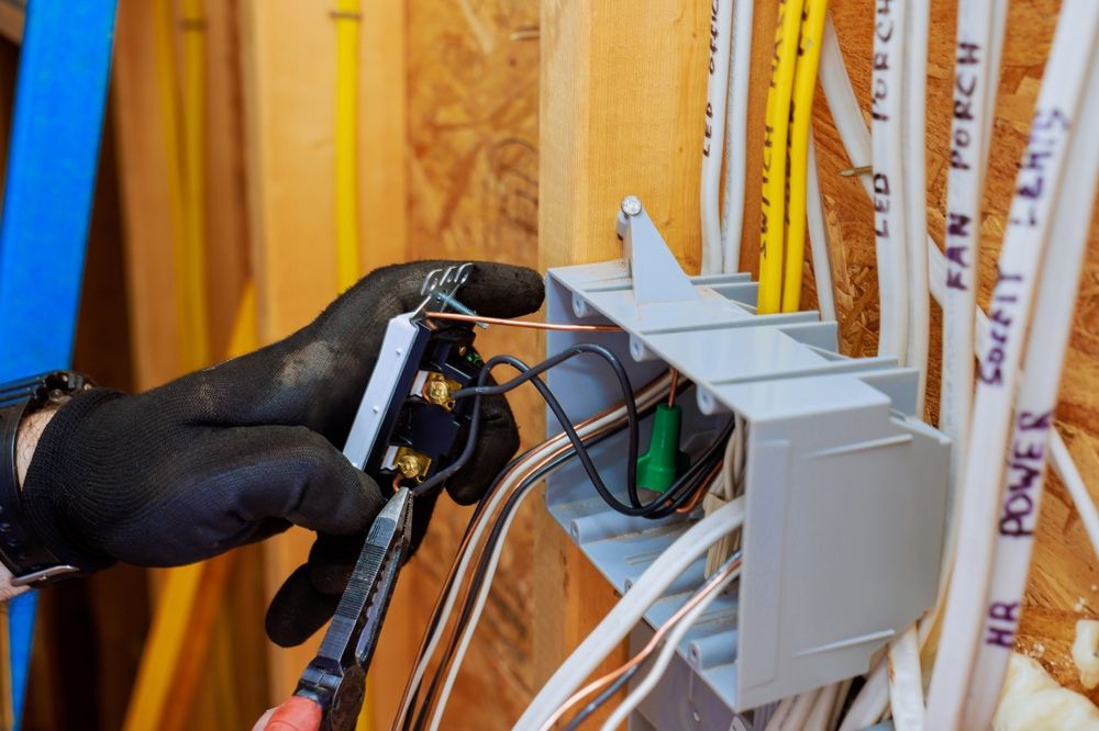 Gloved hand installing cables into a wall-mounted electrical box with exposed wiring