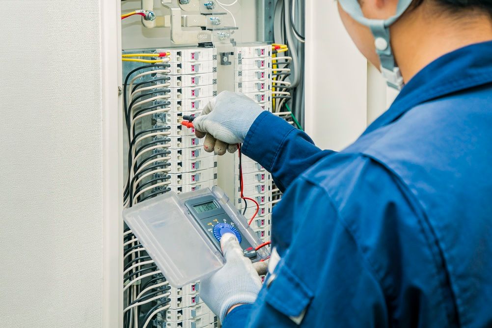 Technician in blue uniform inspecting wiring inside an electrical control panel