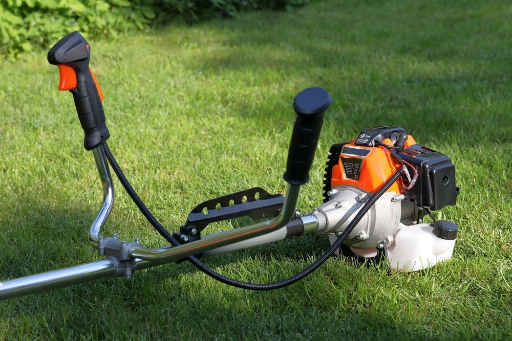 Gas-Powered String Trimmer on A Grassy Lawn, Orange and Black with Metal Handle and Black Grips — Young's Lawn Care In Kelso, QLD