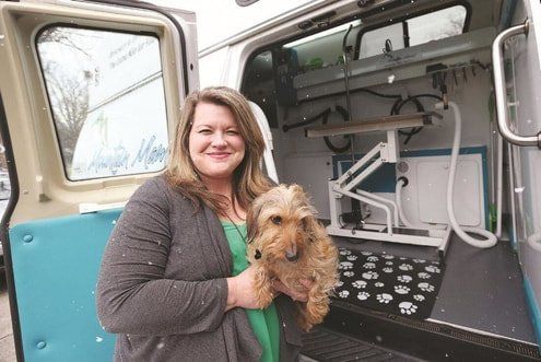 A woman is holding a small dog in front of a van.