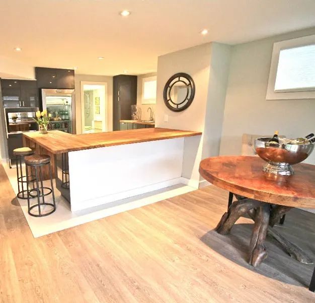 A contemporary kitchen with a light wood floor, white island with a wooden countertop, bar stools, and a round wooden table.