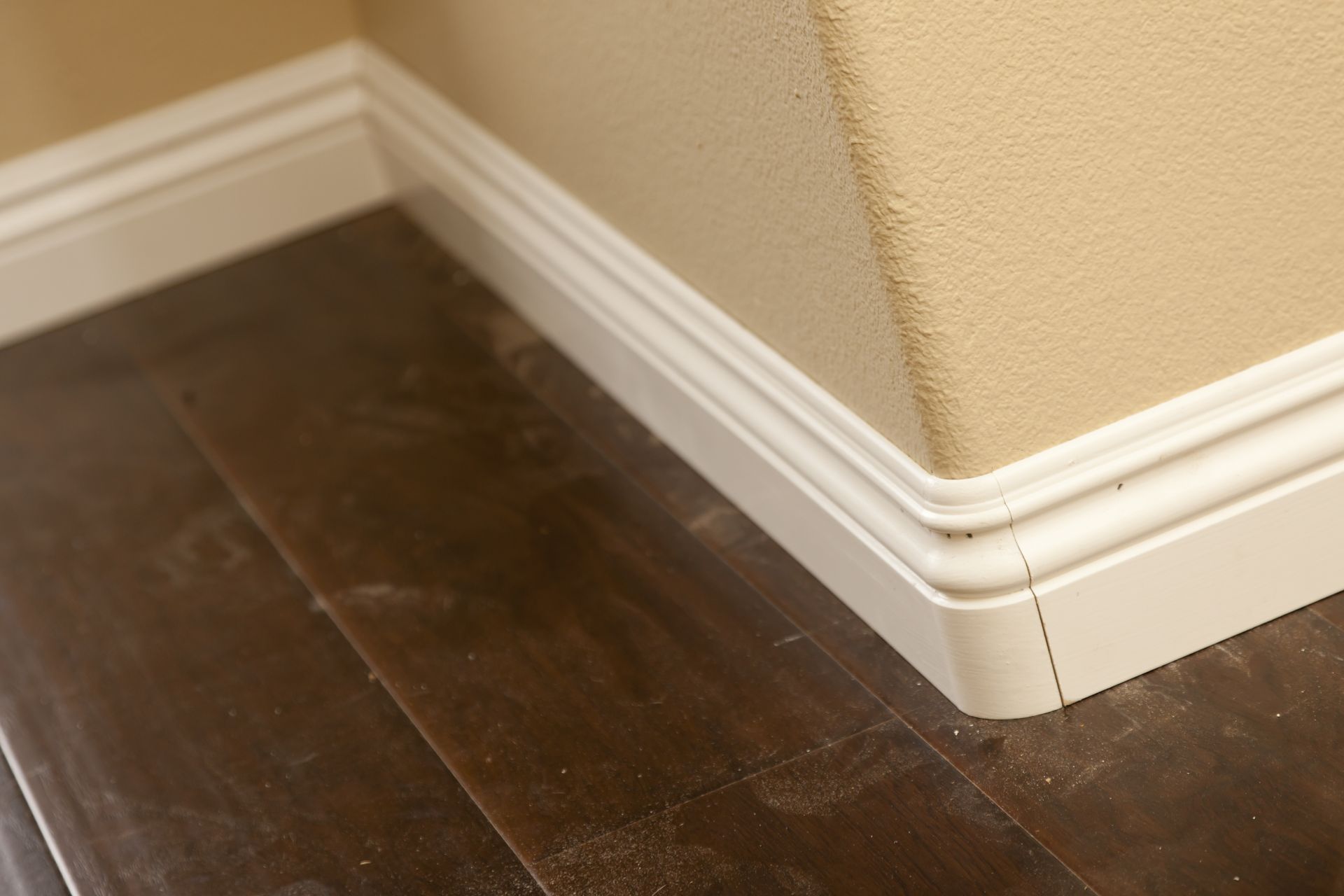 Dark wood floor with white baseboard trim at a beige wall corner.