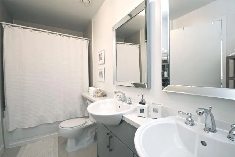 A modern bathroom with a double vanity, white sinks, gray cabinets, two mirrors, and a white shower curtain.