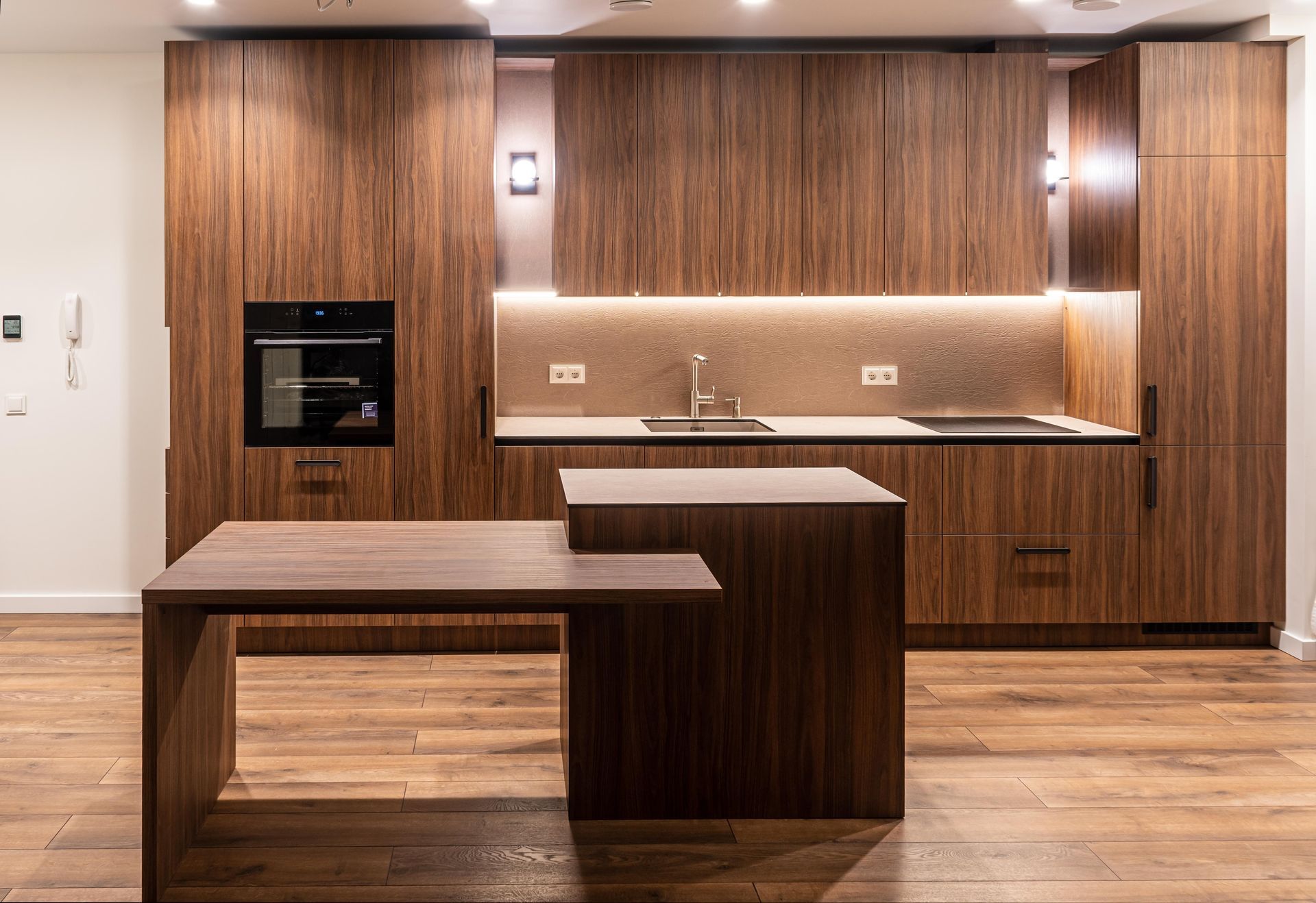 Modern wood kitchen with island, built-in appliances, and warm under-cabinet lighting.