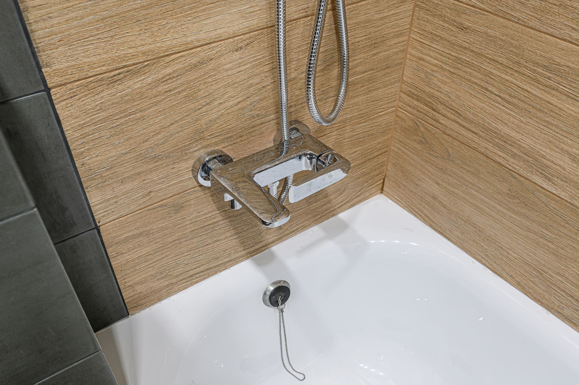 Modern shower with wood-look tile walls, white tub, and chrome handheld showerhead