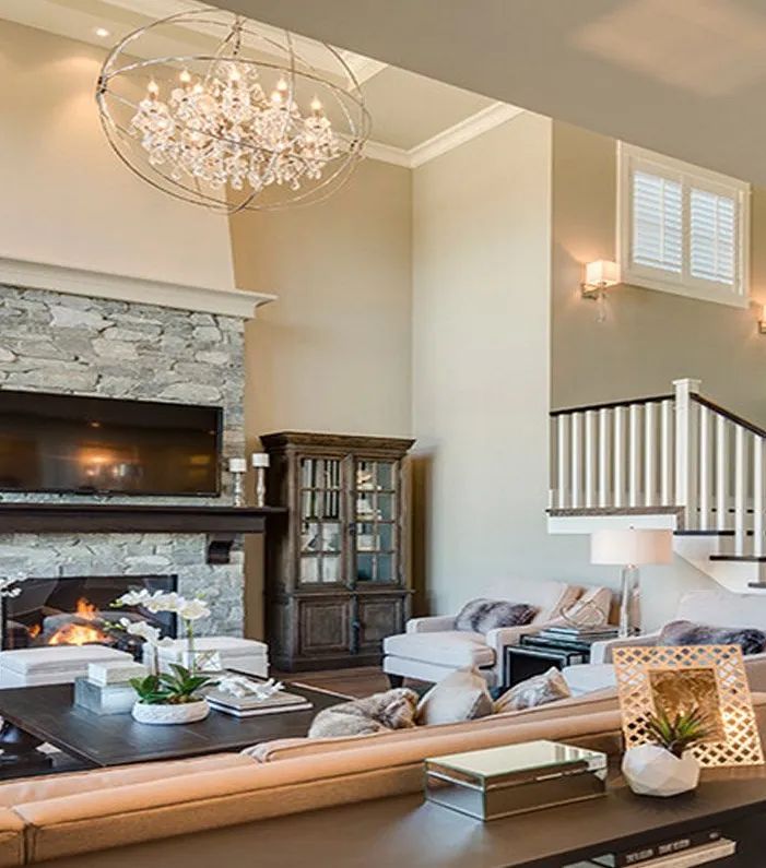 A spacious living room with a stone fireplace, large crystal orb chandelier, dark wood cabinet, and a beige sofa.