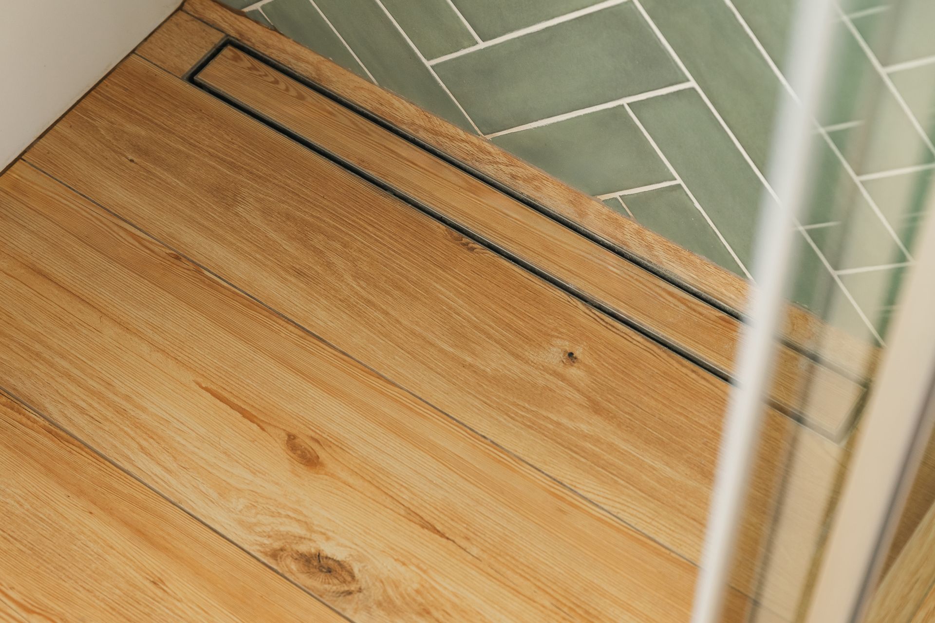 Wooden floor beside a green-tiled shower area with a narrow drain grate.