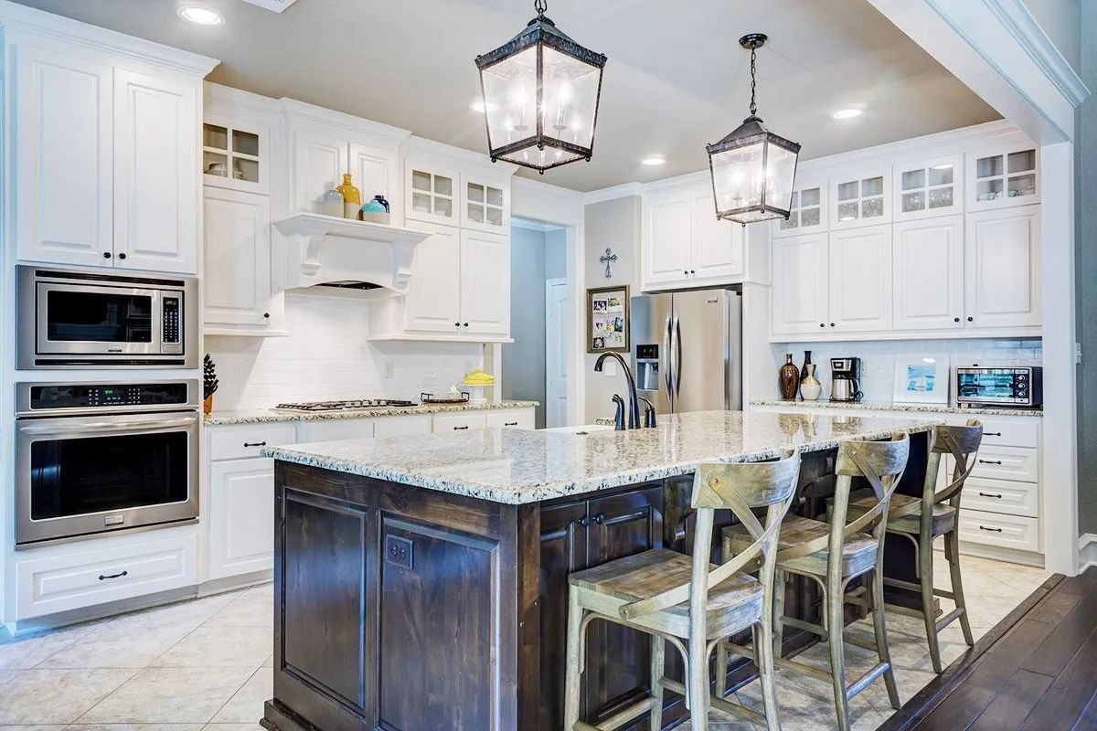 A modern, well-lit kitchen with white cabinetry, stainless steel appliances, a dark wooden island, and two pendant lights.