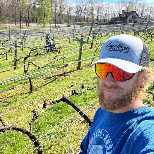 A man wearing a hat and sunglasses is standing in a vineyard.