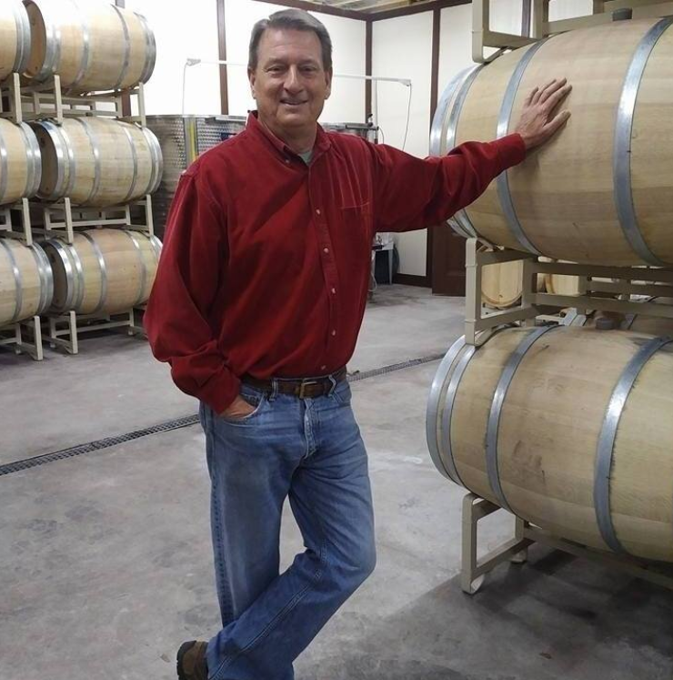 A man in a red shirt leans on a wooden barrel