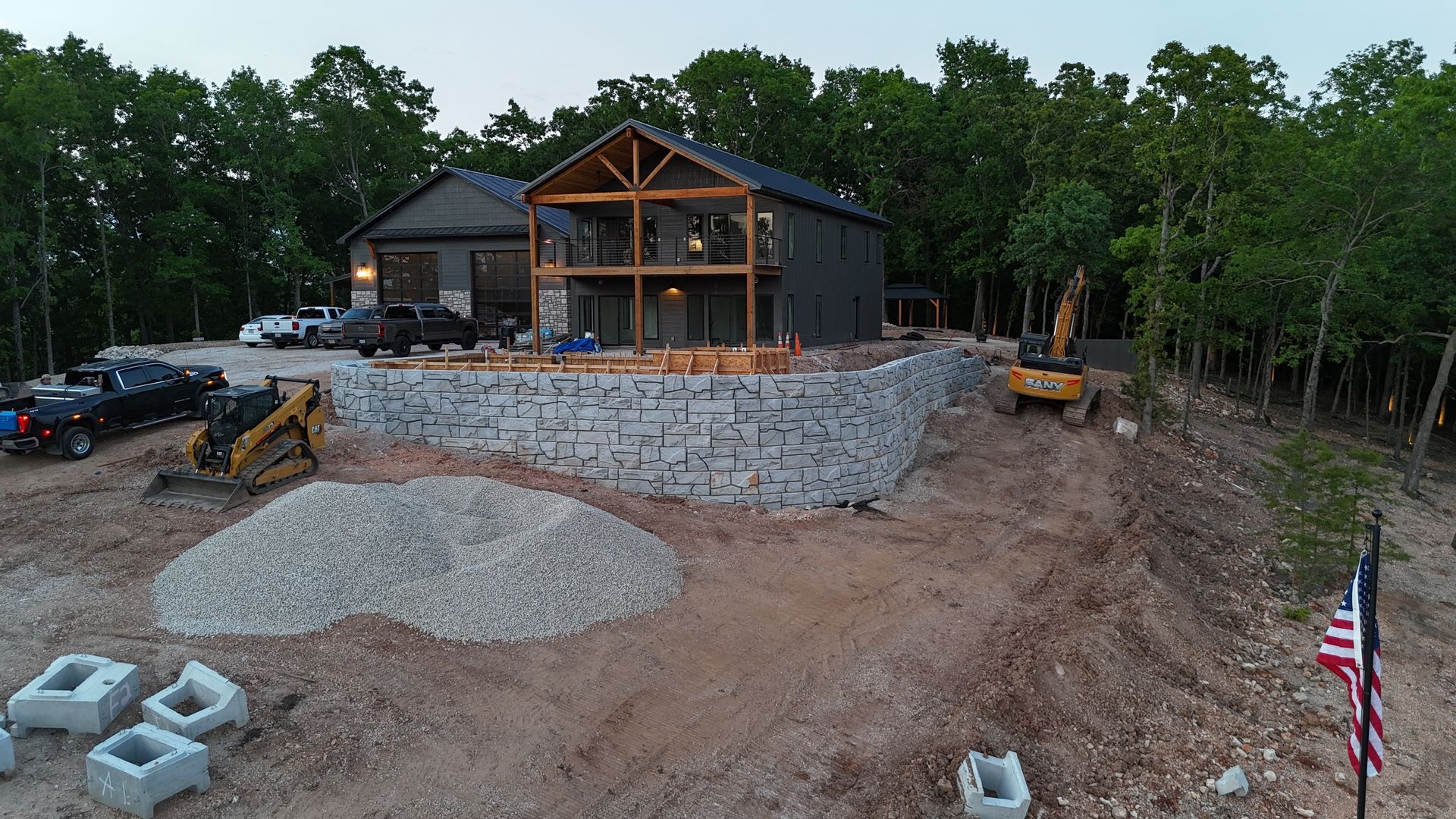 Rural house under construction with stone retaining wall, gravel driveway, and construction equipment nearby
