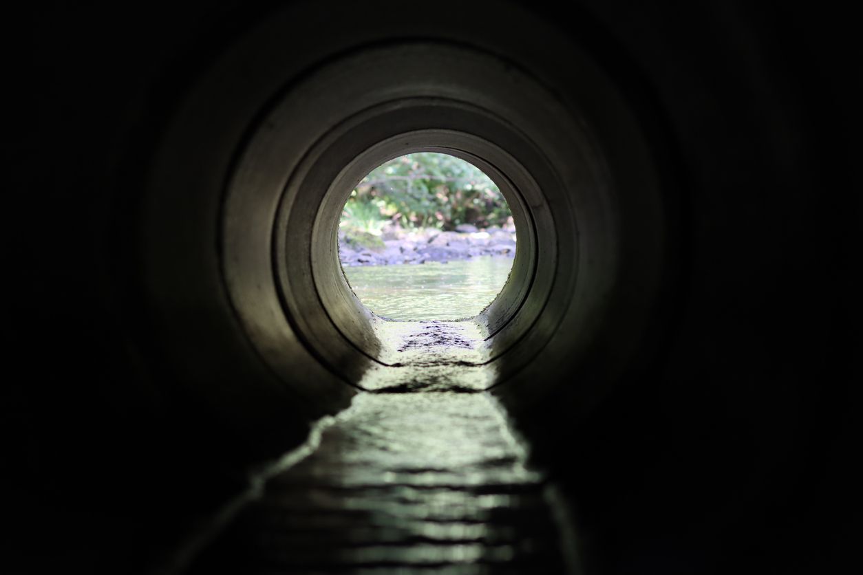 Dark tunnel framing a bright circular opening with water flowing toward it