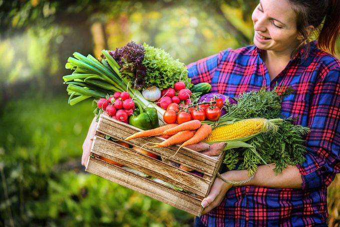 A woman is holding a wooden crate filled with fresh vegetables.