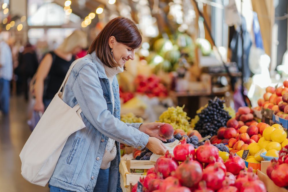 A woman is buying fruits and vegetables at a market.