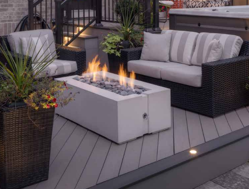 Outdoor patio with a modern fire pit, two wicker sofas, and potted plants.