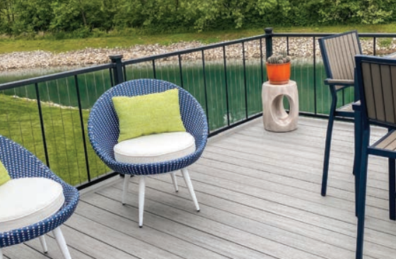 Patio with blue chairs, green pillows, wooden deck, and black railing overlooking water.