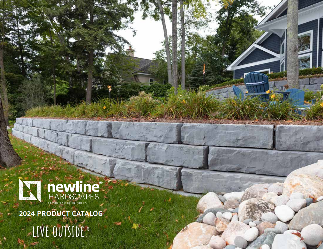 Retaining wall made of gray blocks with a house and greenery in the background.
