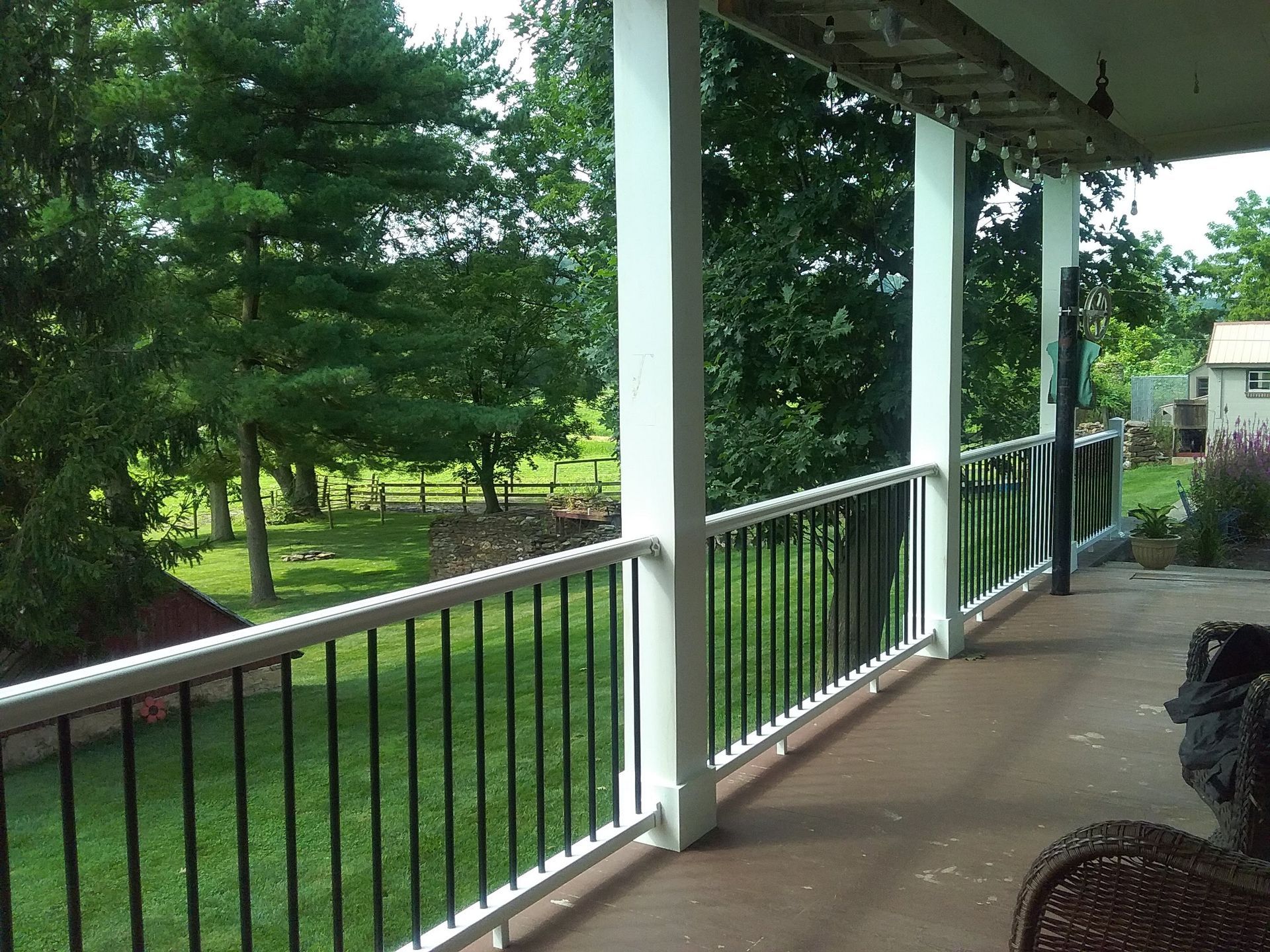 Covered porch with white columns and black railing overlooking a green yard and trees