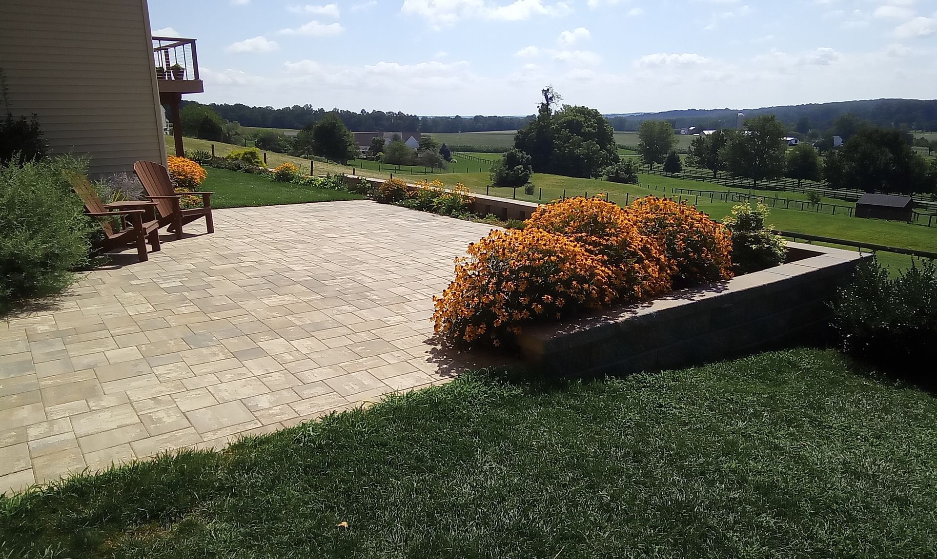 Patio with orange flowers overlooking a green lawn and distant countryside