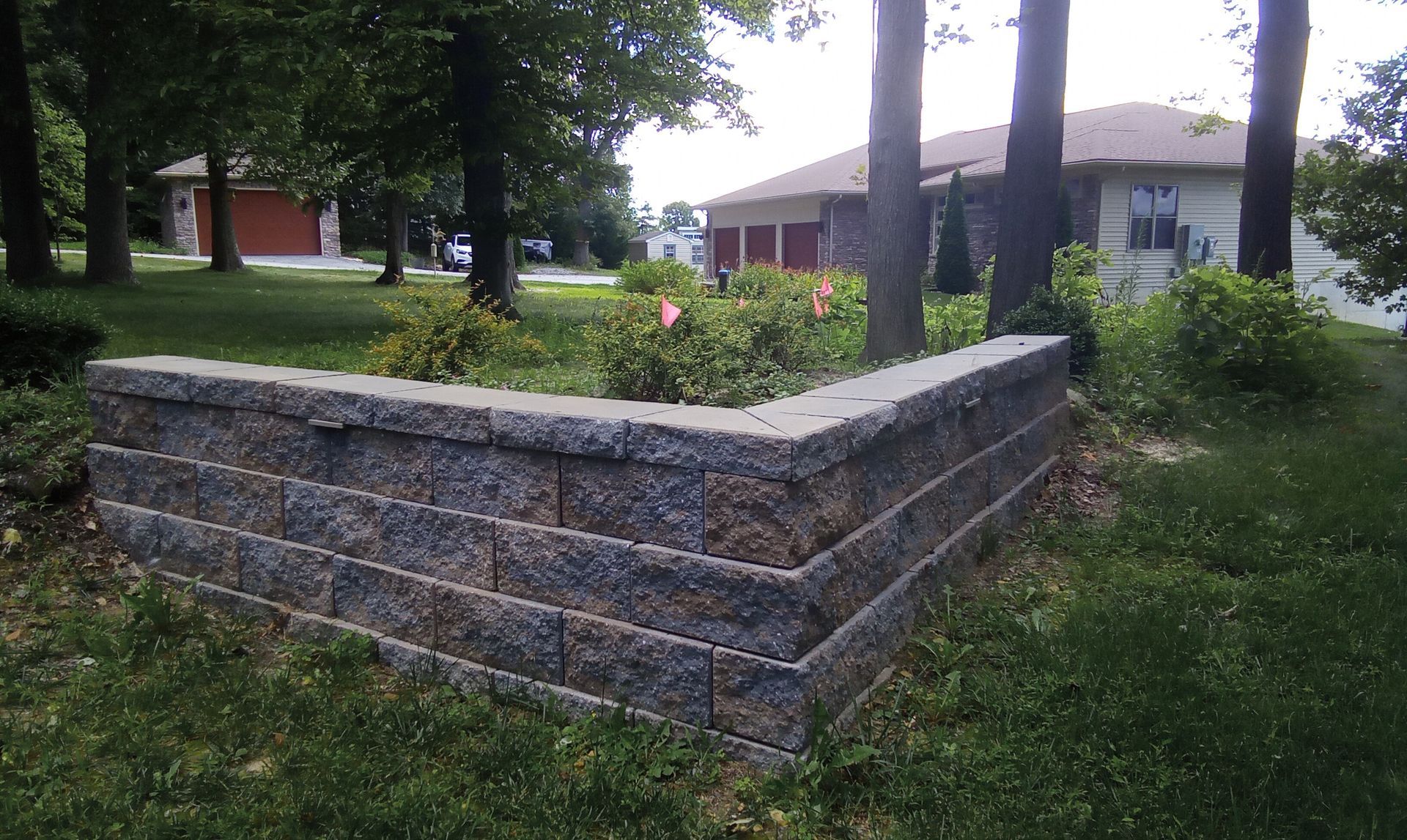 Stone planter wall in a grassy park near trees and a building