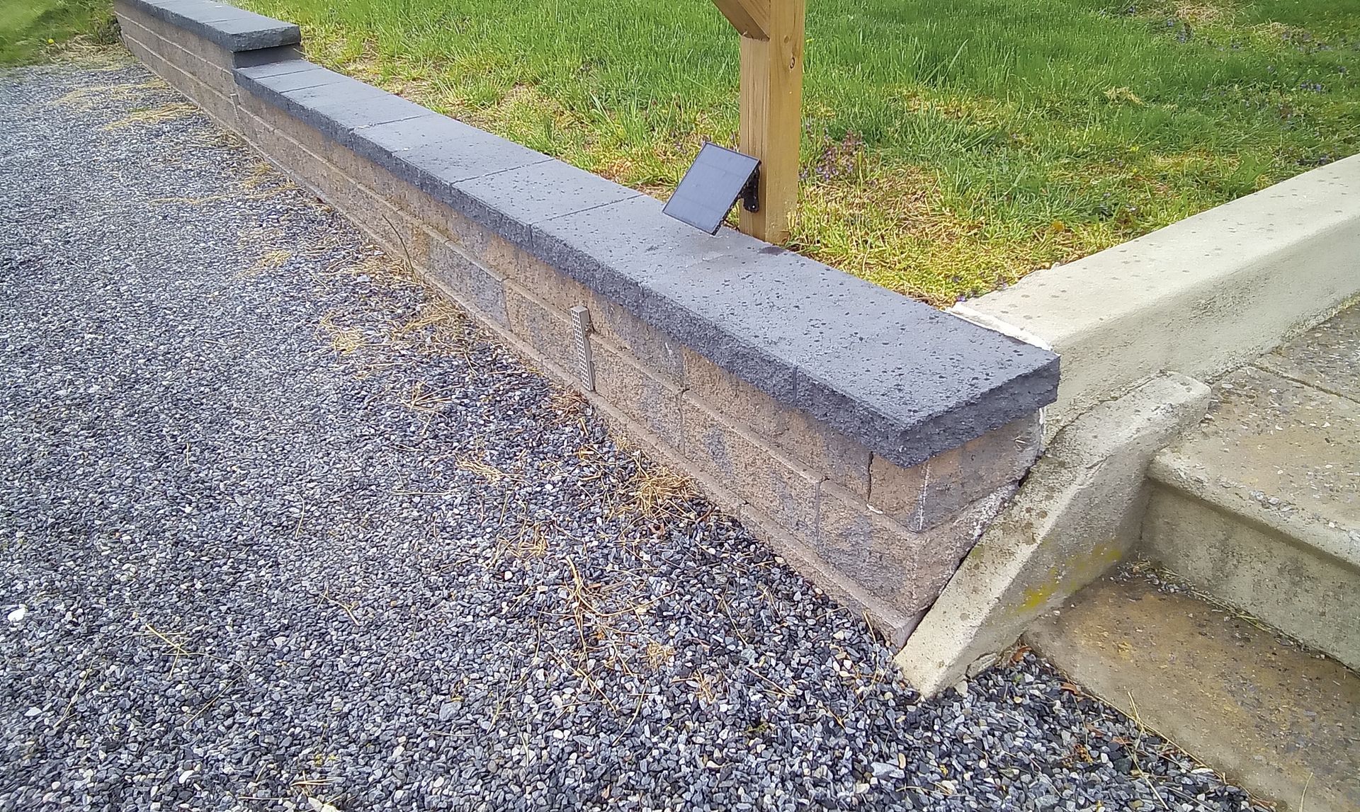 Gravel path beside a raised concrete curb, next to a grass lawn and steps.